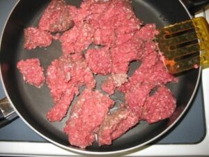 Ground beef in a frying pan with a spatula.