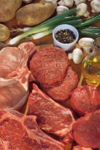 Meats and vegetables on a wooden table.